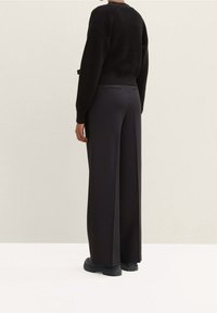 Černý pletený svetr s texturovaným vzorem, spárovaný s černými kalhotami s vysokým pasem a širokými nohavicemi a robustními černými botami.