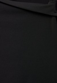 Tissu noir lisse plié dans le coin supérieur droit montrant la texture et le tombé du matériau.