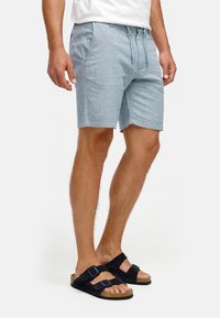 Lichtblauwe, geweven shorts met een koordsluiting in de taille, zijzakken en een ontspannen pasvorm, gecombineerd met zwarte suède sandalen met verstelbare banden.