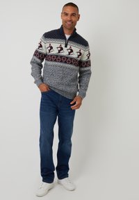 Pullover lavorato a maglia in blu navy con motivo nella parte superiore caratterizzato da bianco, rosso e grigio. Abbinato a jeans blu e sneakers bianche. Texture morbida, vestibilità rilassata.