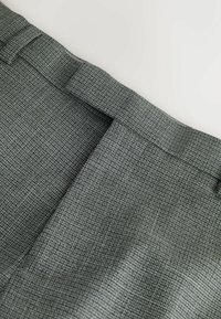 Šedá vzorovaná látka s károvaným dizajnom. Textúra je hladká s pevne tvarovaným pásom a jemnými švami.