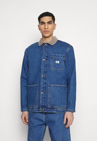 Blauwe spijkerjack met een corduroy kraag, voorkant met knopen, twee grote zakken en een klein logo-opdruk. Textiele stof met zichtbare stiksels.