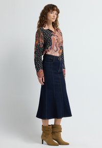 Koszula z długim rękawem w wzory w kolorach czarnym, różowym i pomarańczowym, zestawiona z ciemnoniebieską spódnicą w kształcie litery A. Brązowe zamszowe botki za kostkę z podwiniętymi mankietami.