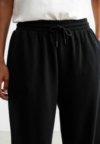 Zwarte sweatpants gemaakt van zacht materiaal, met een elastische tailleband en een trekkoord, evenals zijzakken. Glad textuur, ontspannen pasvorm.