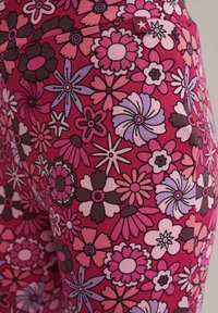 Leggings florale cu un fundal roz vibrant, prezentând diferite flori în nuanțe de mov, roz și maron. Material texturat cu detalii de nervuri.