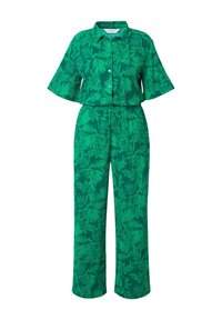 Zelený dvoudílný outfit skládající se z košile s krátkým rukávem a kalhot s širokými nohavicemi, zdobený tropickým listovým vzorem v různých odstínech zelené.