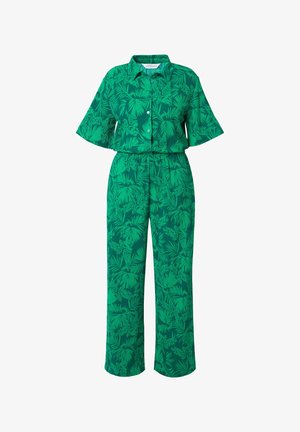 Zelený dvoudílný outfit skládající se z košile s krátkým rukávem a kalhot s širokými nohavicemi, zdobený tropickým listovým vzorem v různých odstínech zelené.