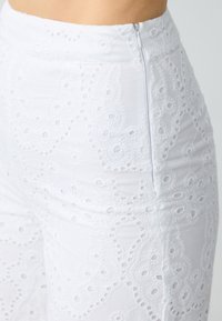 Witte cropped broeken met een textuur, geborduurd bloemenontwerp en uitsnijdingen. Voorzien van een rits aan de zijkant.