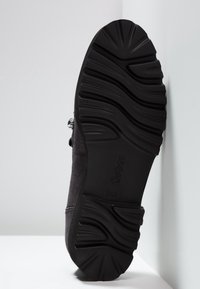 Semelle d'une chaussure noire avec des motifs de semelle profonds et ondulés, estampillée "Gabor", avec un petit détail de boucle métallique visible sur le côté.