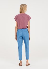 Korte mouwen, mauve top gecombineerd met lichtblauwe, taps toelopende broek. De broek heeft een elastische tailleband en is opgerold bij de enkels.