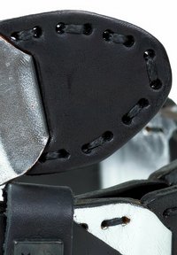 Bracelet en cuir noir avec des accents en métal argenté, présentant des coutures visibles et une surface texturée. Le matériel comprend des sections métalliques brillantes.
