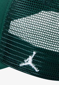 Gorra de color verde oscuro con una parte trasera de malla, visera curvada y logo Jumpman bordado en blanco en la parte frontal. El material muestra una apariencia texturizada.
