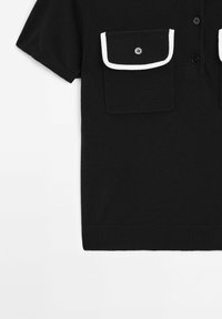 Chemise noire à manches courtes avec fermeture à boutons sur le devant, deux poches poitrine ornées de bordures blanches et boutons noirs.