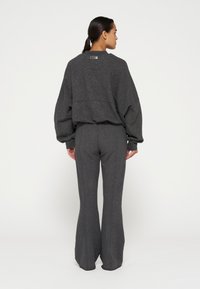 Grijs, textuur sweatoutfit met een losse pullover en flared broek. De trui heeft een label op de rug; de stof heeft een subtiele glans.