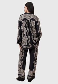 Svart sateng to-delt antrekk med intrikate beige paisley-mønstre. Løs skjorte med lange ermer og vide bukser.