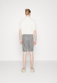 Camicia a maniche corte beige chiaro abbinata a pantaloni corti a quadri grigi, con fascia elastica in vita. Indossata con sabot di colore chiaro.
