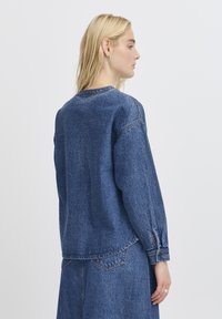 Denimtröja i mörkblått med långa ärmar, rund halsringning och distinkt sömnad. Har en avslappnad passform och sprund på baksidan.