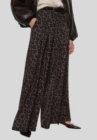 Pantaloni a gamba larga con stampa leopardata in tessuto marrone scuro e nero, caratterizzati da pieghe e vita alta, abbinati a una cintura nera e scarpe con punta.