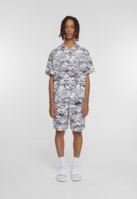 Short-sleeve button-up shirt and shorts set, white with black abstract line pattern, lightweight material, relaxed fit, worn with white slides.