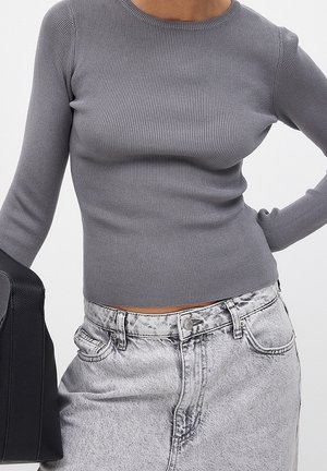 Personne portant un haut gris côtelé ajusté à manches longues et un jean gris délavé taille haute, portant un sac à main noir texturé.