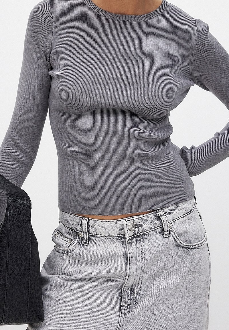 Personne portant un haut gris côtelé ajusté à manches longues et un jean gris délavé taille haute, portant un sac à main noir texturé.