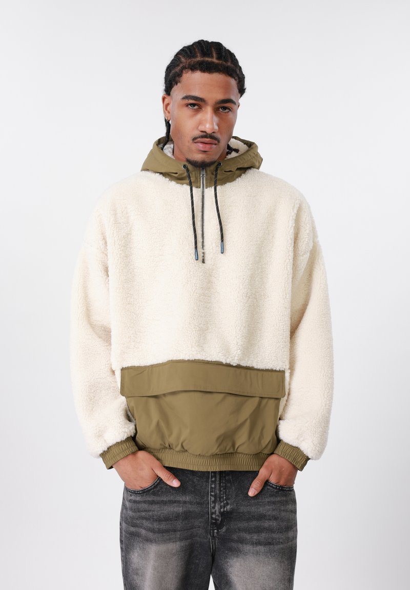 Kremo spalvos vilnos megztinis su alyvuogių žalumos apačios panelė ir kapišonas. Turi elastines rankogalius ir raištelį, taip pat kengūros kišenę.