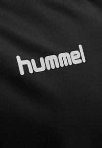 Mustan kankaan pintakuvio, jossa on valkoinen "hummel"-logo pyöreässä kirjasintyypissä, esillä selvästi.
