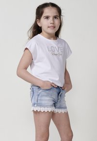 Balta īsām piedurknēm T-kreklā ar zeltā drukātu tekstu "LOVE" un "Kereishi Girl". Gaiši zilas džinsu šortus ar baltu mežģīņu apdari apakšā.