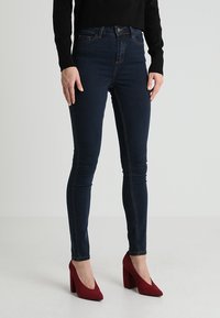 Námořnické skinny džíny z denimu s vysokým pasem, s kontrastním prošíváním. Spárovány s červenými lodičkami pro větší kontrast.