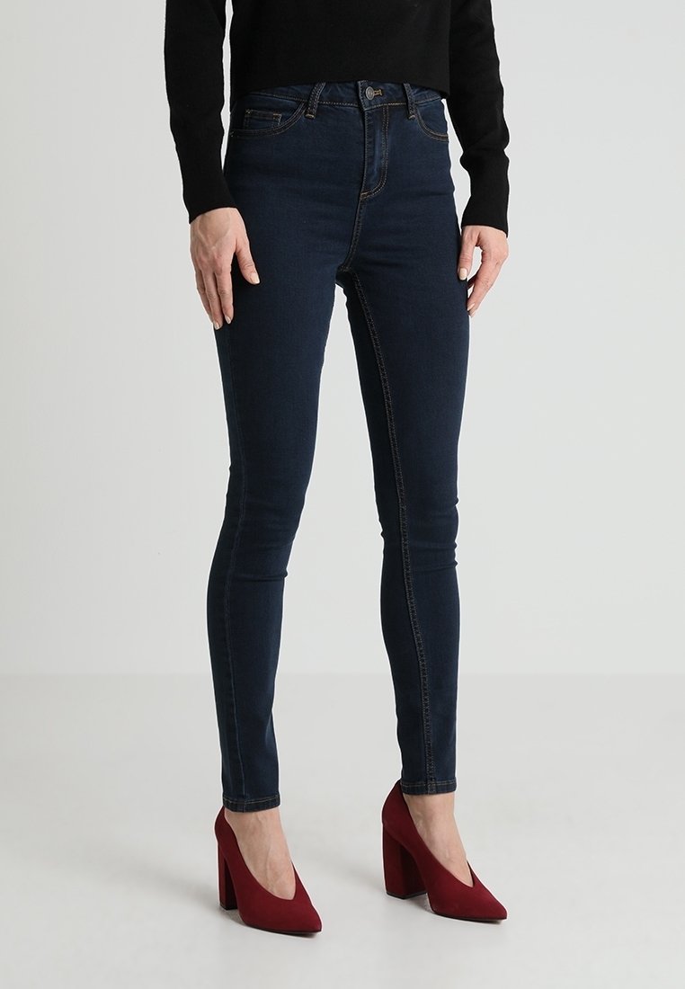 Námořnické skinny džíny z denimu s vysokým pasem, s kontrastním prošíváním. Spárovány s červenými lodičkami pro větší kontrast.