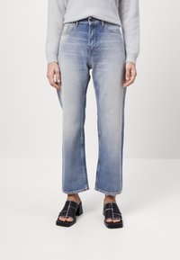 Světle modré džíny s vysokým pasem, rovného střihu, s vybledlým vzhledem a surovým lemem. V kombinaci s černými sandály na podpatku.