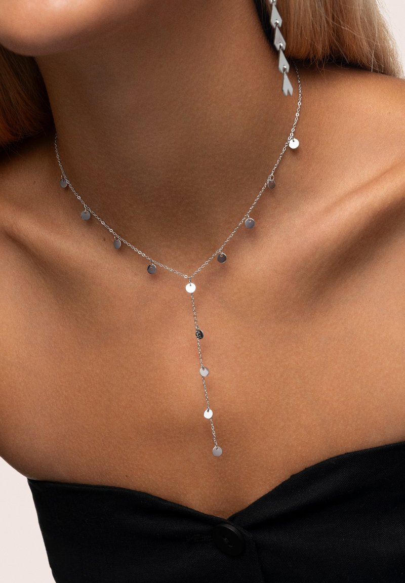 Collana in argento con pendenti circolari, caratterizzata da un design delicato e a forma di Y, posata sulla pelle nuda.