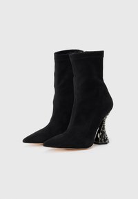 Cizme negre din suede, la glezna, cu vârf ascuțit și toc înalt, sculptat, având un accent texturat negru. Partea superioară netedă cu un design fără cusături.