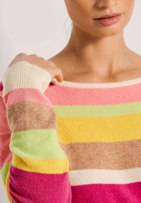 Multikleurige gestreepte trui met roze, gele, groene en bruine strepen, voorzien van een zachte textuur en een crèmekleurige ribbelkraag en manchetten.