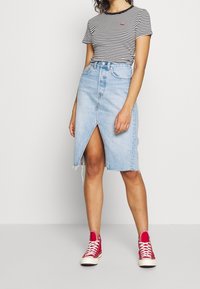 Gonna di denim in azzurro chiaro con orlo sfilacciato e spacco frontale. Abbinata a una t-shirt a righe nere e sneakers alte rosse.