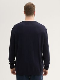 Un pull à manches longues bleu marine avec col rond, bords-côtes aux poignets et à l'ourlet. Texture douce avec un design uni, coutures visibles sur les épaules.