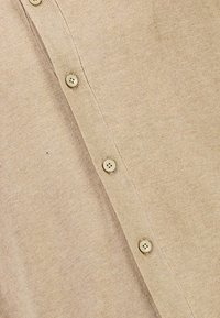 Beige cardigan med ribbad struktur, som har en rad av sex matchande knappar framme och en slät, mjuk tygfinish.