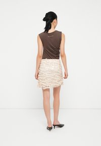 Haut sans manches marron avec une finition texturée, associé à une jupe en dentelle rose clair présentant des motifs ondulés, et des mules à talons noirs.