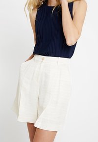 Haut sans manches bleu marine plissé associé à un short crème texturé taille haute avec fermeture à bouton et poches latérales.