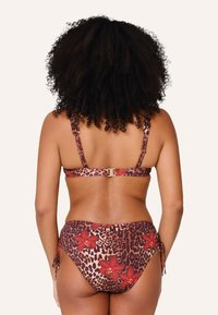 Bikini de estampado de leopardo con acentos florales rojos; presenta tirantes ajustables y un cierre dorado. La tela tiene un acabado suave y texturizado.