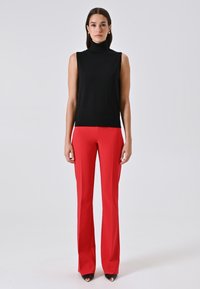 Zwarte mouwloze coltrui gecombineerd met rode op maat gemaakte broek, met een aansluitende silhouet en gladde texturen, compleet met zwarte hakken.