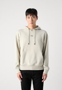 Sudadera de color beige claro, hecha de tejido suave, con un bolsillo tipo canguro, capucha con cordón y logo negro "BOSS" en el pecho.