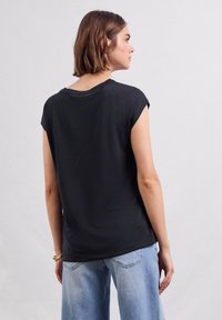 Černý krátký rukáv top s uvolněným střihem, kulatým výstřihem a strukturovanou tkaninou, kombinovaný se světle modrými širokými džínami.