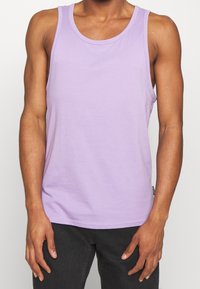 Lila bomullstopp med rund halsringning. Har en slät yta utan synliga mönster eller designs. Bärs med mörka byxor.