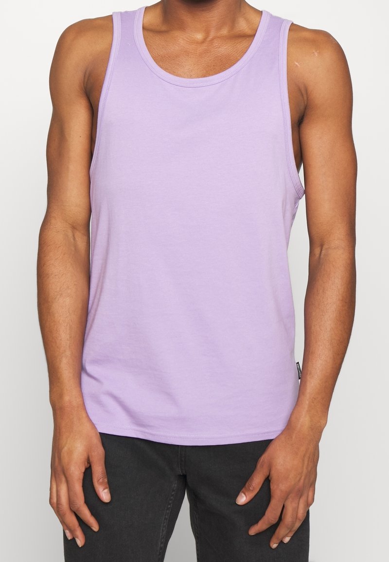 Lila bomullstopp med rund halsringning. Har en slät yta utan synliga mönster eller designs. Bärs med mörka byxor.