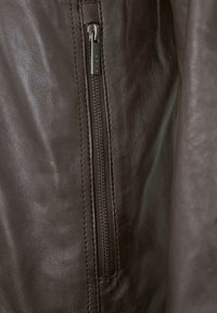 Nahaufnahme eines Reißverschlusses einer braunen Lederjacke mit sichtbaren Nähten und strukturiertem Ledermaterial.