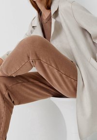 Lys beige skræddersyet jakke over et brunt sæt, der har blødt stof og slim-fit design. Glat tekstur med subtile sømme.