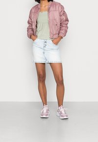 Chaqueta bomber rosa claro, blusa verde con fruncidos, minifalda de mezclilla clara con botones y zapatillas rosas con acentos blancos. Texturas suaves.