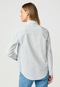 Camicia a maniche lunghe azzurro chiaro a righe, realizzata in tessuto con una texture liscia. Con colletto a punta e orlo arrotondato.