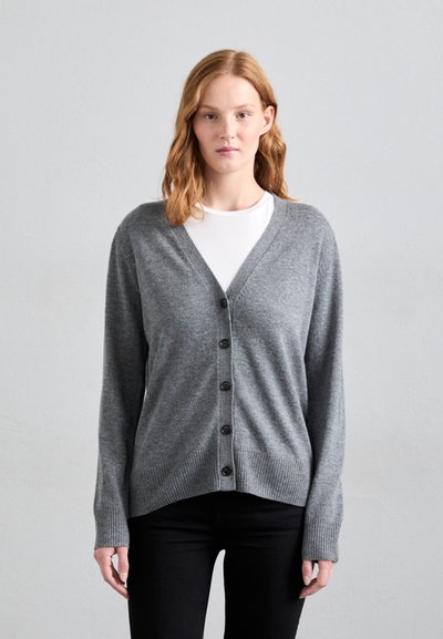 Grijze cardigan van zacht materiaal, met een v-hals, lange mouwen, zes zwarte knopen en geribbelde boorden en onderkant. Geselecteerd over een wit shirt.